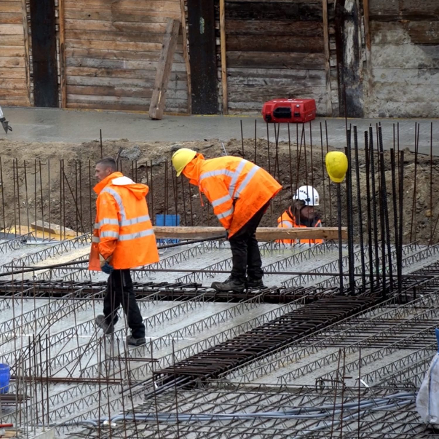 Construction workers in orange vests and hard hats working on a concrete foundation.