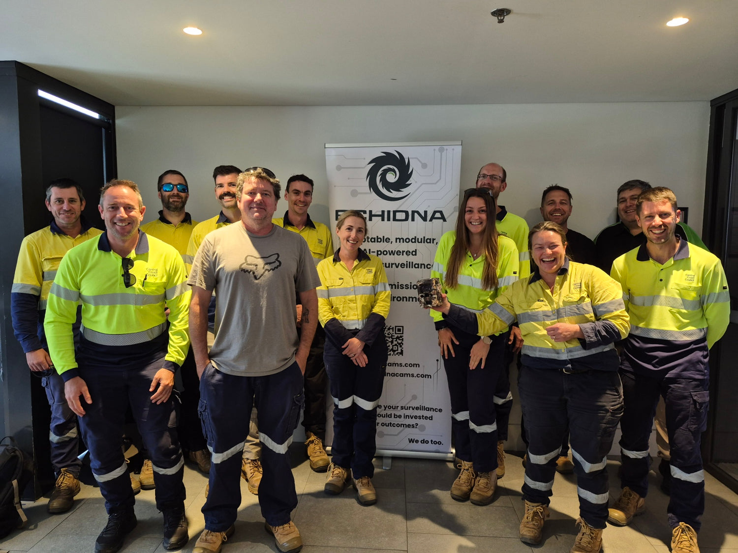 Group of people in high-visibility safety gear posing in front of an Echidna sign.